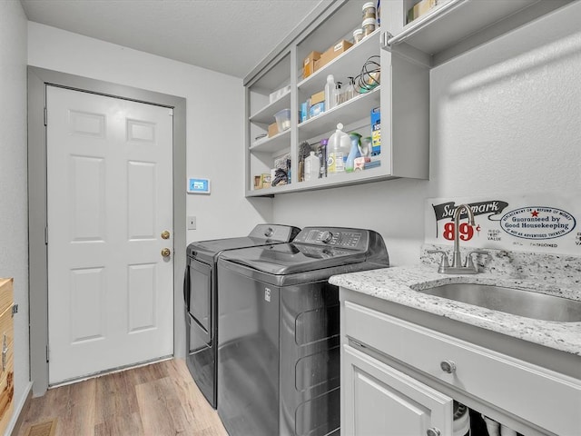 laundry room with light wood-type flooring, separate washer and dryer, and sink