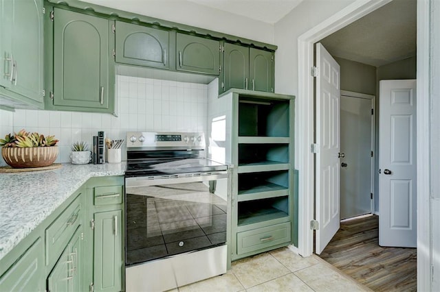 kitchen with stainless steel electric stove, decorative backsplash, green cabinets, and light tile patterned flooring