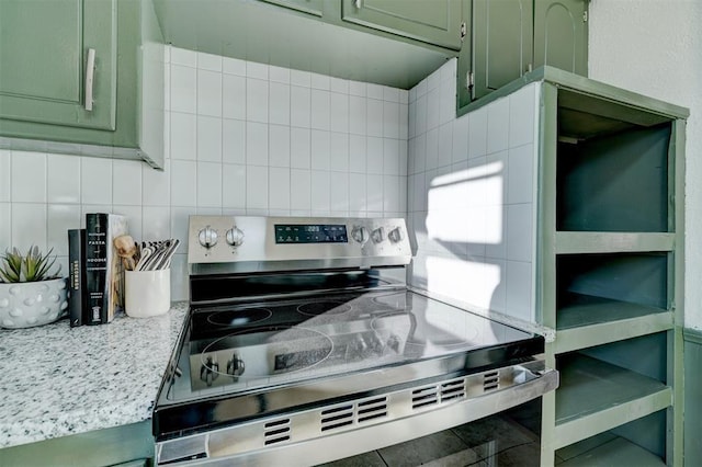 kitchen with stainless steel electric stove, decorative backsplash, green cabinets, and light stone countertops