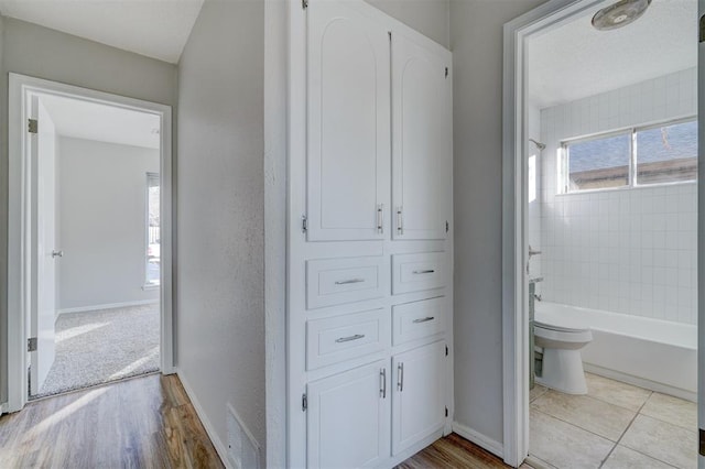 bathroom with tiled shower / bath combo, hardwood / wood-style flooring, and toilet