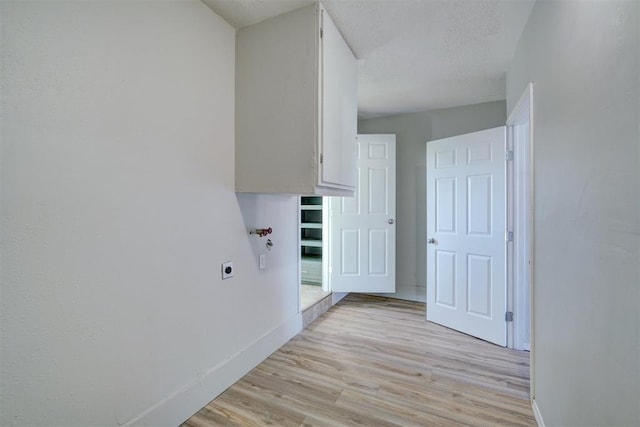 clothes washing area featuring hookup for an electric dryer, a textured ceiling, and light hardwood / wood-style flooring