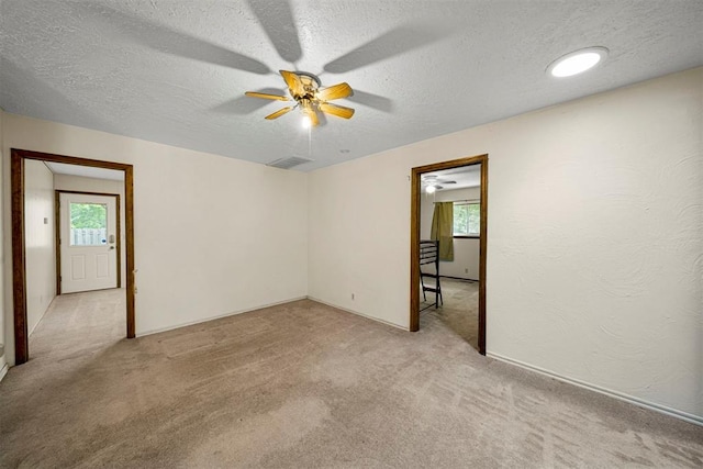 unfurnished room featuring ceiling fan, light colored carpet, and a textured ceiling