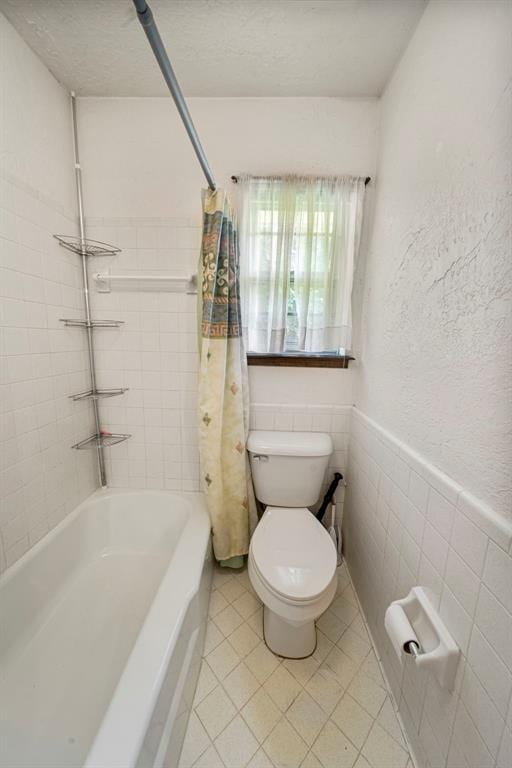 bathroom featuring a textured ceiling, toilet, tile walls, and shower / bath combo with shower curtain