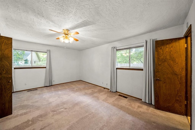 carpeted empty room featuring a wealth of natural light, ceiling fan, and a textured ceiling