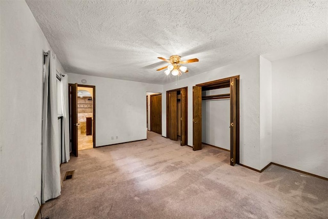 unfurnished bedroom with light carpet, a textured ceiling, ceiling fan, and multiple closets