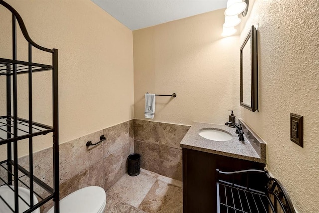 bathroom featuring vanity, toilet, and tile walls