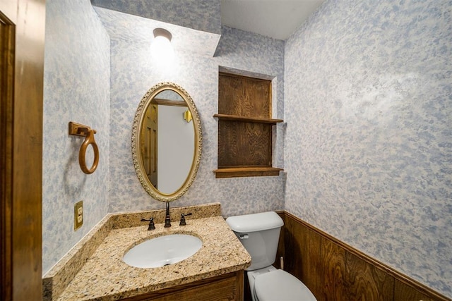 bathroom featuring wooden walls, vanity, and toilet