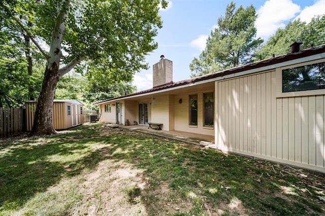 back of property with a lawn, a patio, and a shed