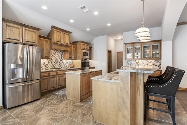 kitchen featuring a kitchen island with sink, pendant lighting, light stone counters, and appliances with stainless steel finishes