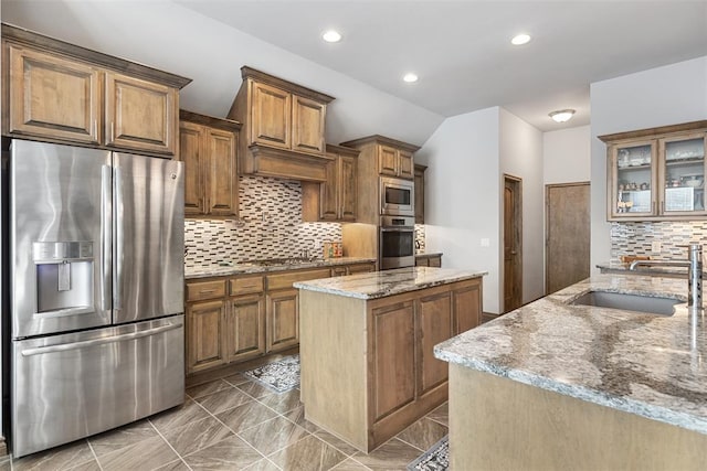 kitchen with appliances with stainless steel finishes, tasteful backsplash, light stone counters, sink, and a center island