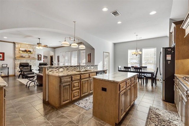 kitchen featuring ceiling fan with notable chandelier, sink, decorative light fixtures, a center island, and stainless steel refrigerator