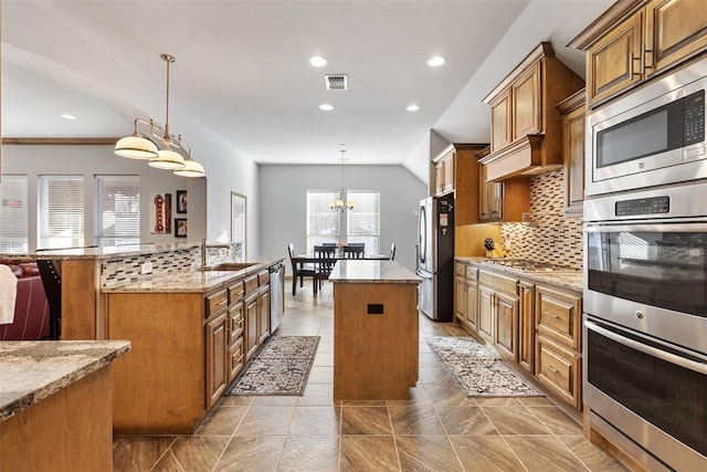 kitchen featuring light stone countertops, sink, stainless steel appliances, decorative light fixtures, and a kitchen island