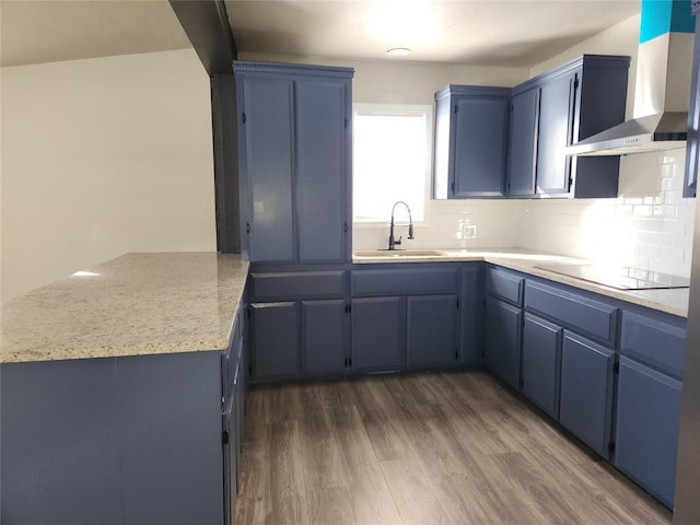 kitchen with wall chimney exhaust hood, decorative backsplash, sink, blue cabinetry, and black electric cooktop