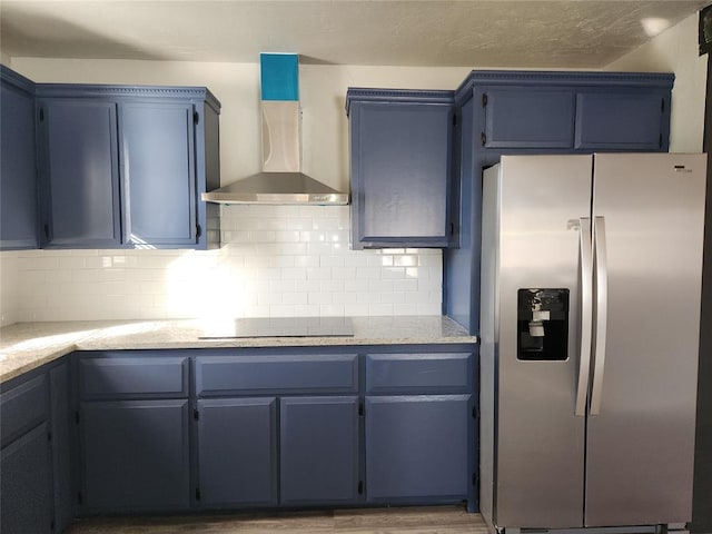 kitchen featuring wall chimney range hood, stainless steel fridge, black electric cooktop, and blue cabinets