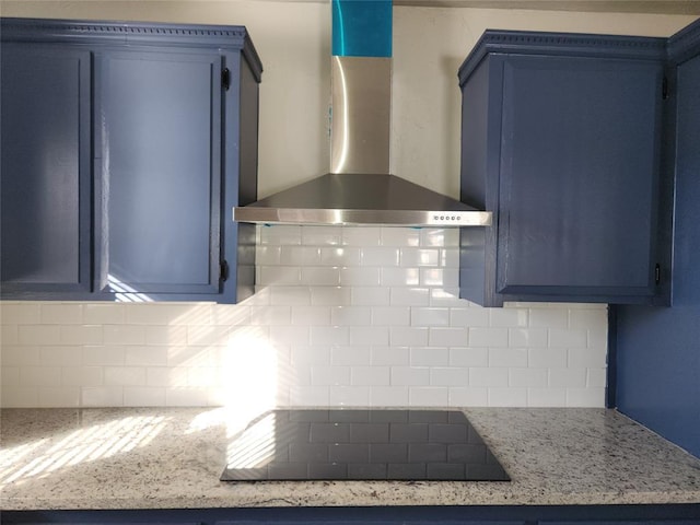 kitchen with tasteful backsplash, black electric stovetop, blue cabinetry, wall chimney exhaust hood, and light stone counters