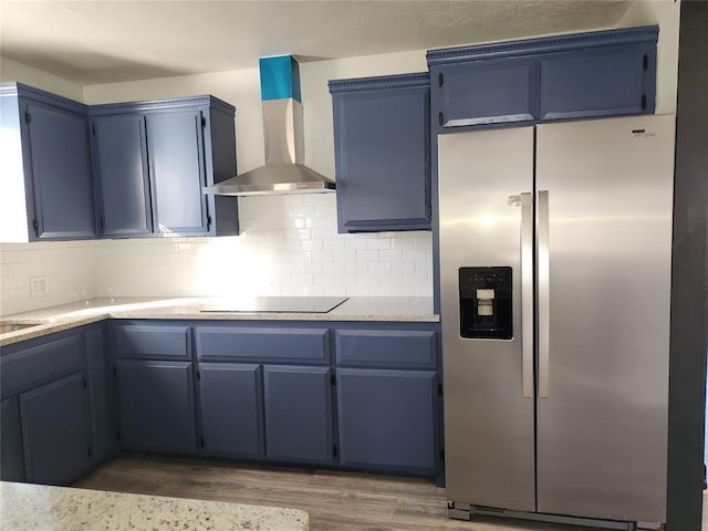 kitchen with stainless steel fridge, black electric cooktop, dark hardwood / wood-style flooring, blue cabinets, and wall chimney exhaust hood