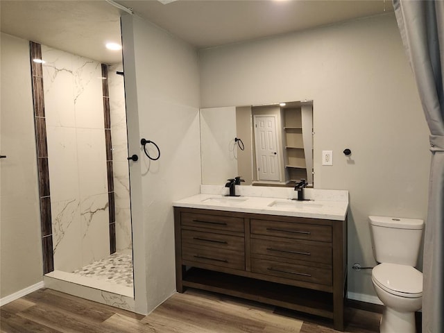 bathroom featuring wood-type flooring, toilet, vanity, and a tile shower