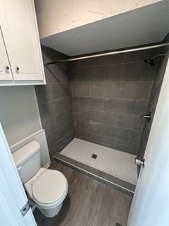 bathroom featuring tiled shower, wood-type flooring, and toilet