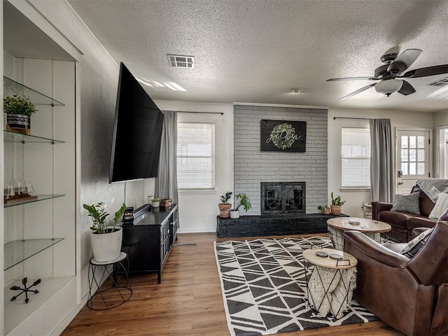 living room featuring wood-type flooring, a textured ceiling, ceiling fan, and a fireplace