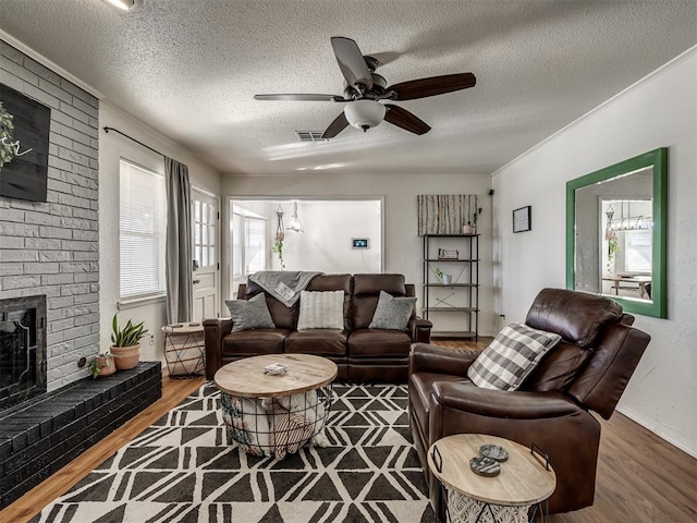 living room featuring ceiling fan, a fireplace, ornamental molding, wood-type flooring, and a textured ceiling