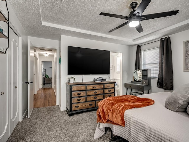 carpeted bedroom featuring ceiling fan, connected bathroom, a textured ceiling, and a tray ceiling