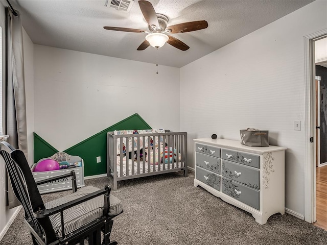 carpeted bedroom with a nursery area, ceiling fan, and a textured ceiling