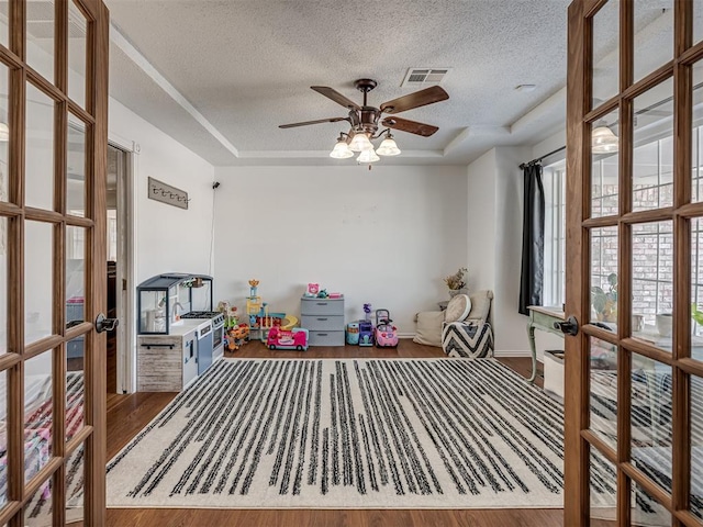 playroom with french doors, a raised ceiling, a textured ceiling, and hardwood / wood-style flooring