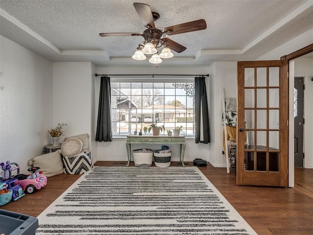 interior space with dark wood-type flooring, ceiling fan, a raised ceiling, and a textured ceiling