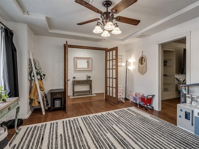 sitting room with ceiling fan, dark hardwood / wood-style floors, a raised ceiling, and a textured ceiling