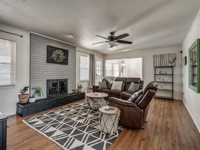 living room featuring ceiling fan, hardwood / wood-style floors, a brick fireplace, and a textured ceiling