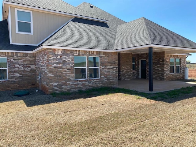 rear view of house featuring a patio area, brick siding, and roof with shingles