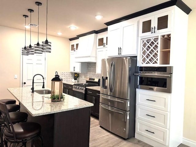 kitchen featuring glass insert cabinets, premium range hood, white cabinetry, appliances with stainless steel finishes, and a center island with sink