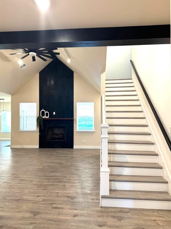 stairs with lofted ceiling with beams, a fireplace, wood finished floors, and a ceiling fan