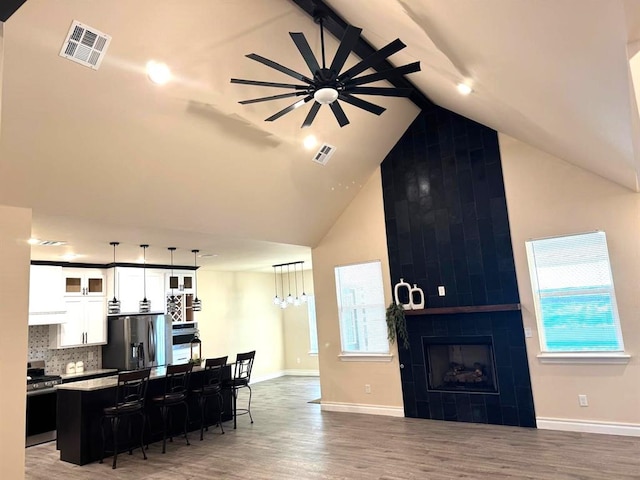 interior space featuring high vaulted ceiling, visible vents, a fireplace, and wood finished floors