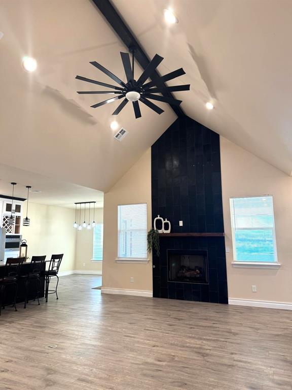 living area with visible vents, a ceiling fan, a tiled fireplace, beamed ceiling, and wood finished floors