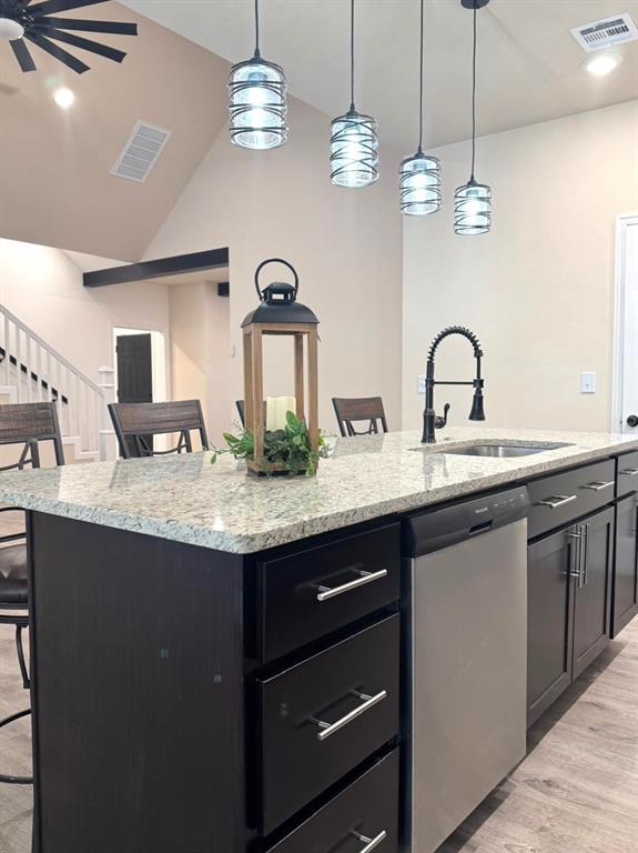 kitchen with a kitchen island with sink, a sink, dark cabinets, dishwasher, and a kitchen bar