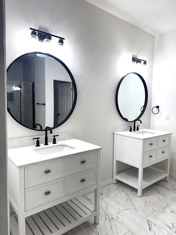 full bathroom with marble finish floor, two vanities, a sink, and baseboards