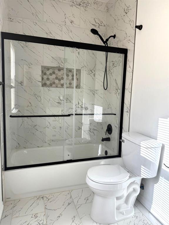 full bathroom with marble finish floor, toilet, and bath / shower combo with glass door