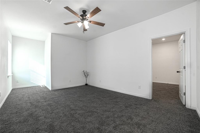 spare room with a ceiling fan, dark carpet, and baseboards