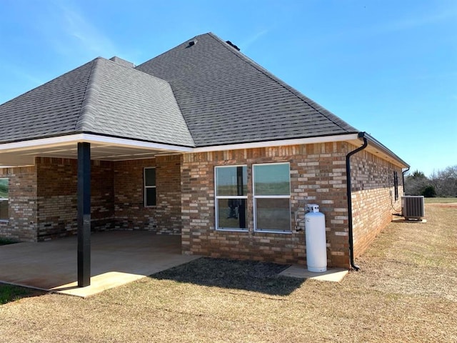 rear view of house with a shingled roof, cooling unit, brick siding, and a patio