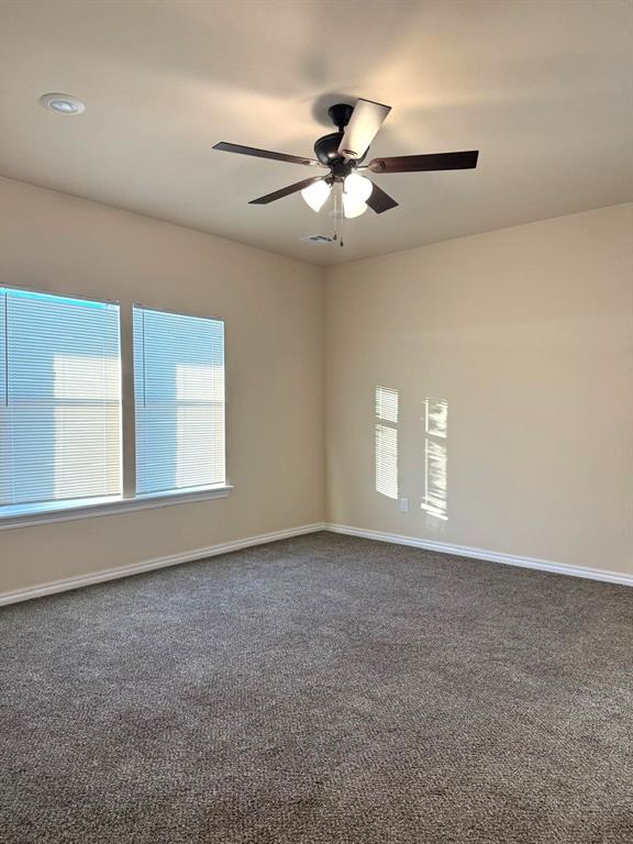 unfurnished room with dark carpet, a ceiling fan, and baseboards