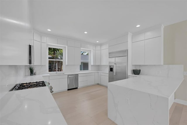 kitchen with light stone counters, light hardwood / wood-style flooring, decorative backsplash, white cabinets, and appliances with stainless steel finishes