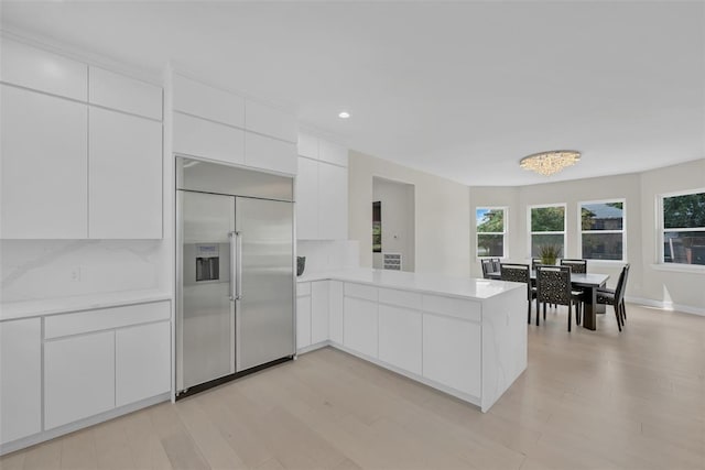 kitchen with white cabinets, stainless steel built in fridge, kitchen peninsula, and an inviting chandelier