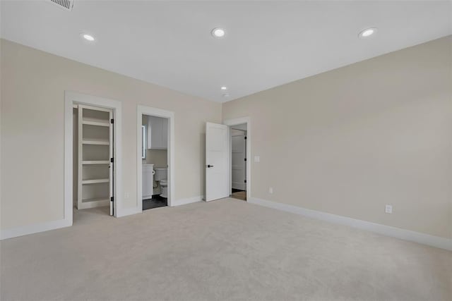 unfurnished bedroom featuring light colored carpet, a spacious closet, connected bathroom, and a closet