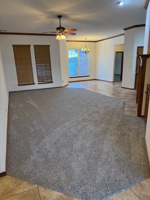 unfurnished living room with ceiling fan with notable chandelier, tile patterned floors, and crown molding