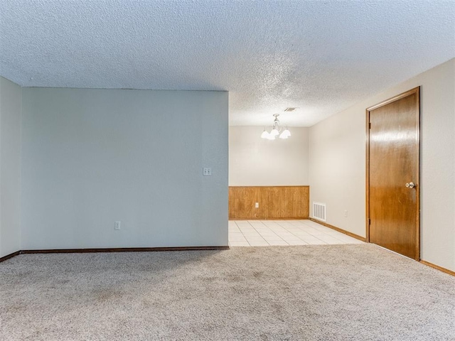 empty room with a textured ceiling, a chandelier, and light colored carpet