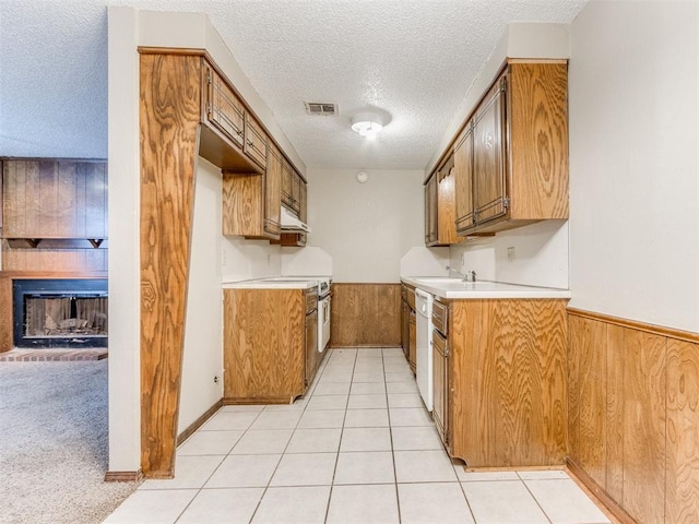 kitchen featuring dishwasher, wood walls, light colored carpet, and a textured ceiling