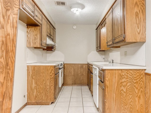 kitchen featuring dishwasher, sink, light tile patterned floors, a textured ceiling, and wooden walls