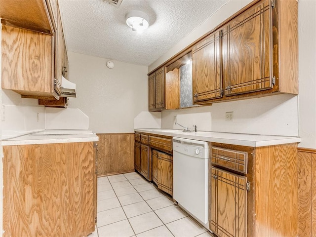 kitchen featuring a textured ceiling, sink, wood walls, white dishwasher, and light tile patterned floors