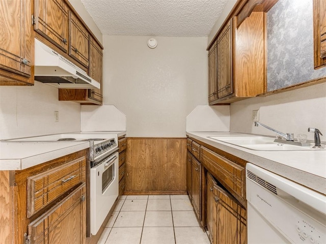 kitchen with white appliances, a textured ceiling, wooden walls, sink, and light tile patterned flooring